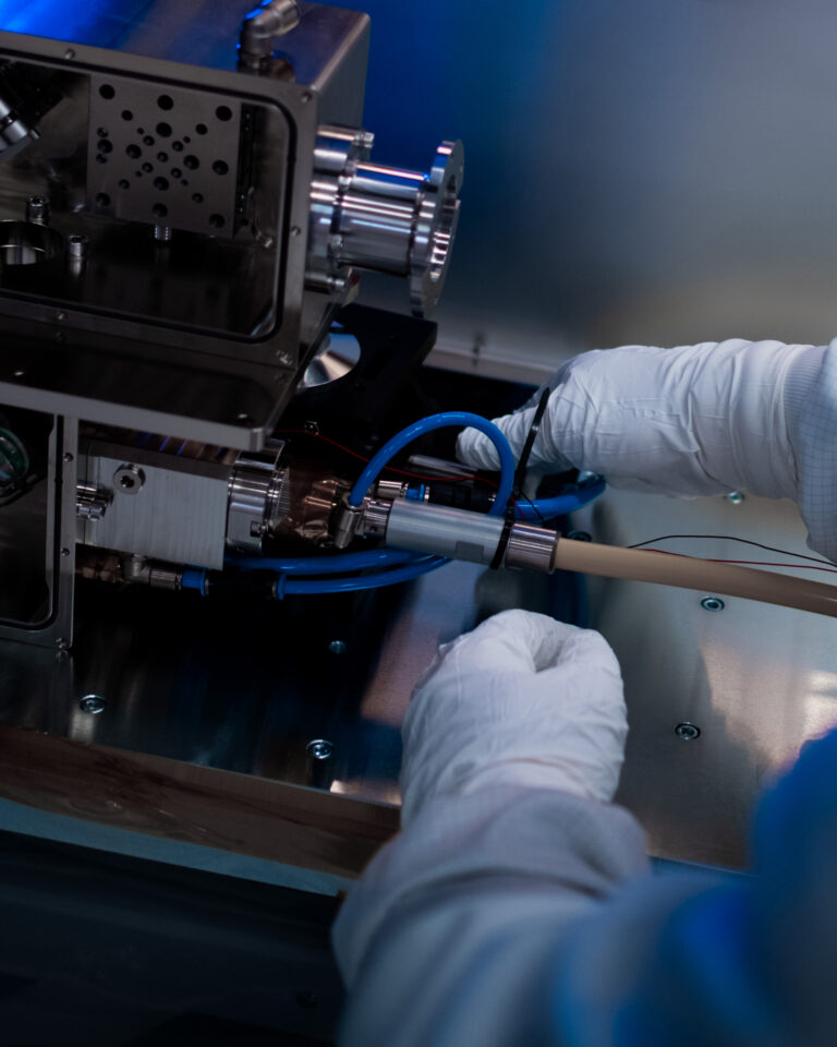 An employee wearing gloves assembles a laser system in a cleanroom environment.
