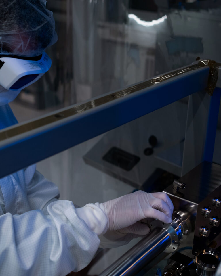 An employee wearing cleanroom attire adjusts a laser unit in a cleanroom environment.